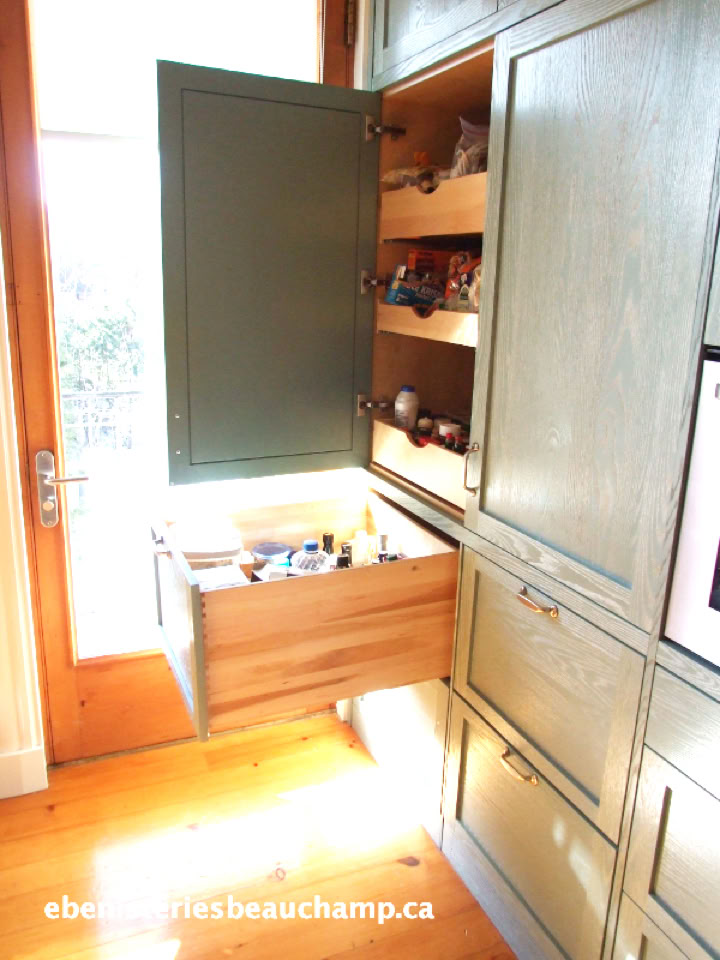A kitchen cabinet with an open drawer and open door, revealing shelves with various items inside.