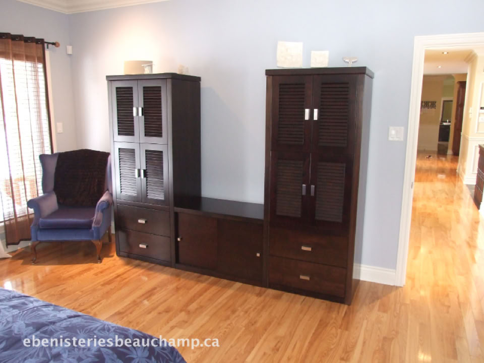 Une pièce avec un sol en bois, une armoire sombre, un fauteuil bleu et une porte ouverte menant à un autre espace.