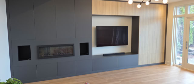Mur avec télévision et cheminée intégrée, entouré de panneaux en bois sombre et clair, avec un lustre moderne au plafond et des portes vitrées à droite.
