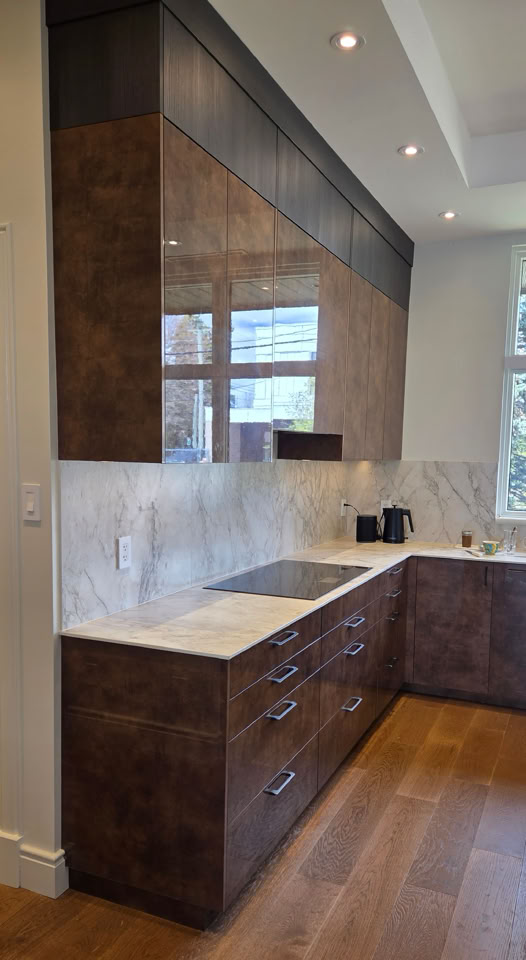 Modern kitchen with dark wood cabinets, marble countertops, electric stovetop, and wooden flooring.