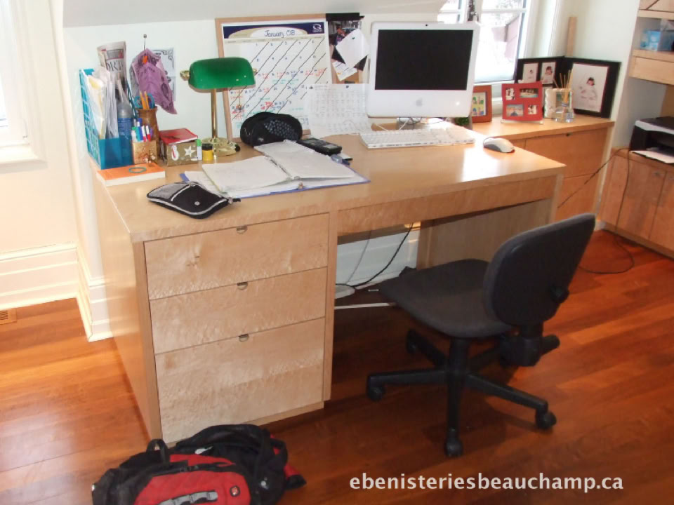 Bureau en bois avec ordinateur, lampe verte, chaise noire, et divers objets de bureau sur un plancher en bois.