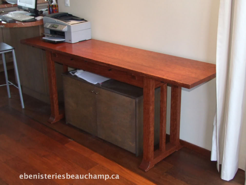 Table en bois avec une imprimante posée dessus, un meuble de rangement en dessous, et un rideau blanc à droite.