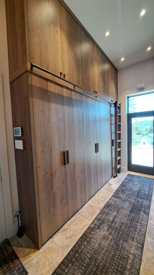 Wooden sliding door with handles in a hallway, adjacent to a windowed door and a small window above.
