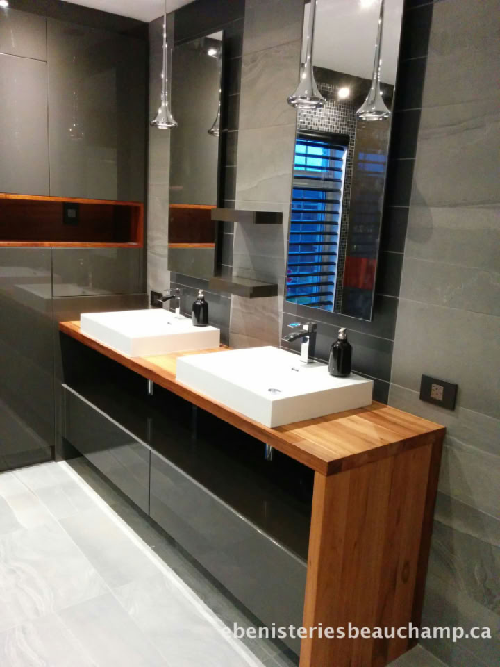 Salle de bain moderne avec deux lavabos blancs sur un comptoir en bois, miroirs au-dessus, et éclairage suspendu.