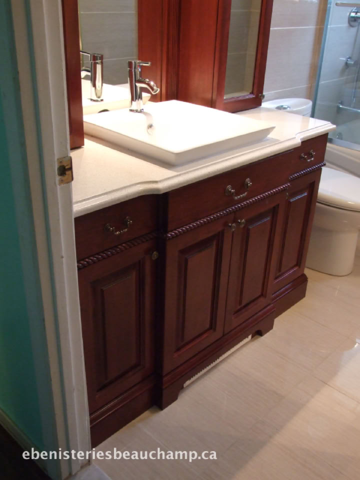 Meuble de salle de bain en bois avec un lavabo blanc et un robinet, miroir au-dessus, toilettes à droite.