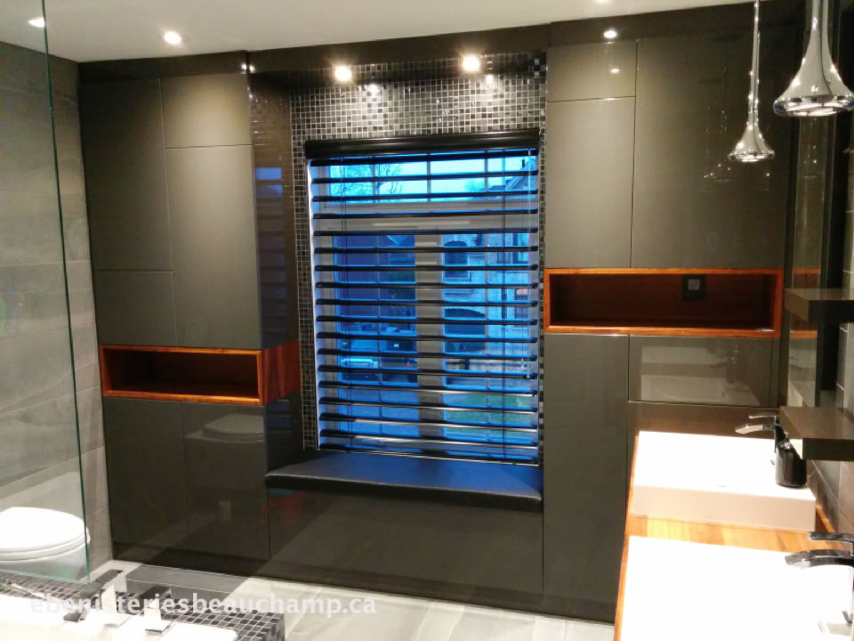 Salle de bain moderne avec un mur sombre, une fenêtre avec des stores horizontaux, un lavabo blanc et des luminaires suspendus.