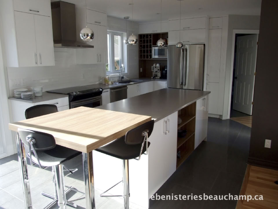 Modern kitchen with a large island, stainless steel appliances, white cabinets, and a wooden dining table with two chairs.