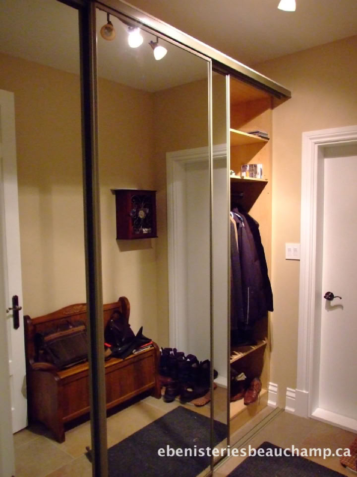 A hallway with a mirrored sliding closet door, a wooden bench with shoes underneath, a coat rack with jackets, and a small wall-mounted shelf.