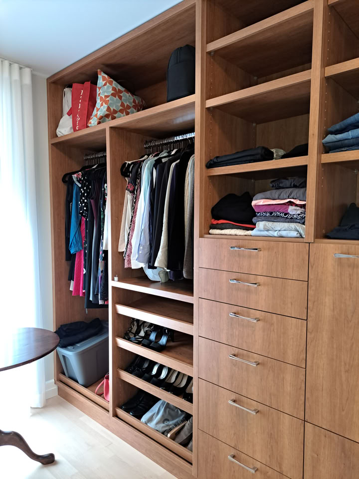 Wooden wardrobe with open shelves and drawers, containing clothes, shoes, and bags.