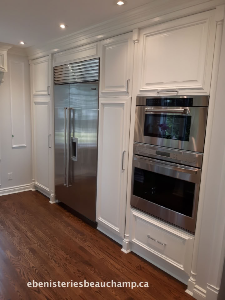 Kitchen with white cabinetry, a stainless steel refrigerator, and built-in ovens.