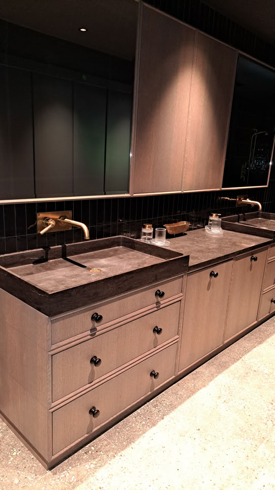 Meuble de salle de bain avec deux lavabos, robinetterie dorée, tiroirs en bois clair et grand miroir au-dessus.