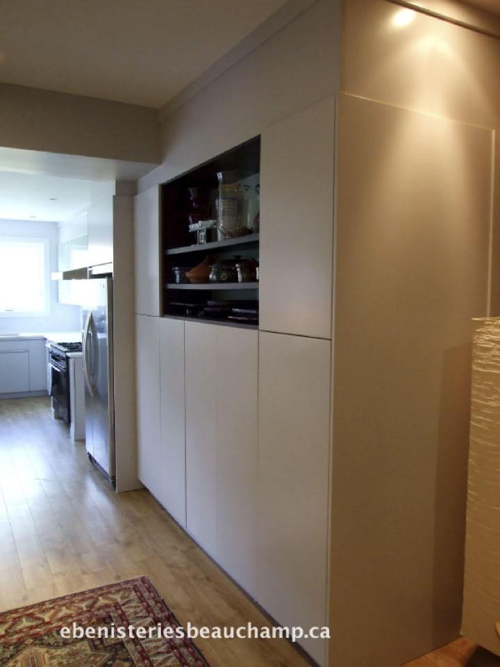 A modern kitchen with light wood flooring, white cabinets, and a built-in shelf displaying dishes.