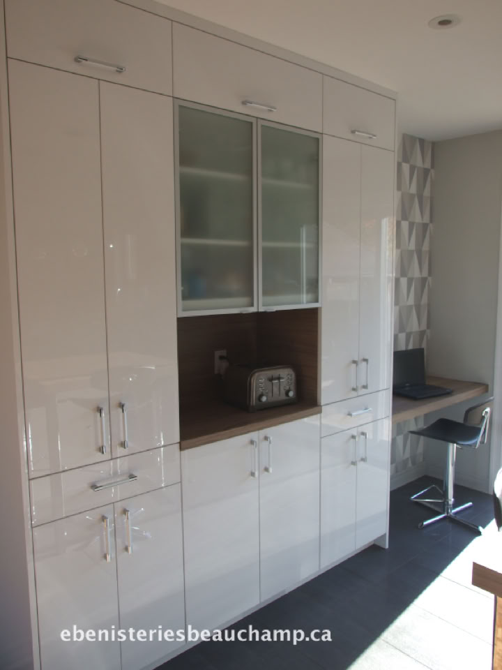 White kitchen cabinets with glass doors in the upper center, a small toaster on a wooden shelf, and a desk area with a chair to the right.