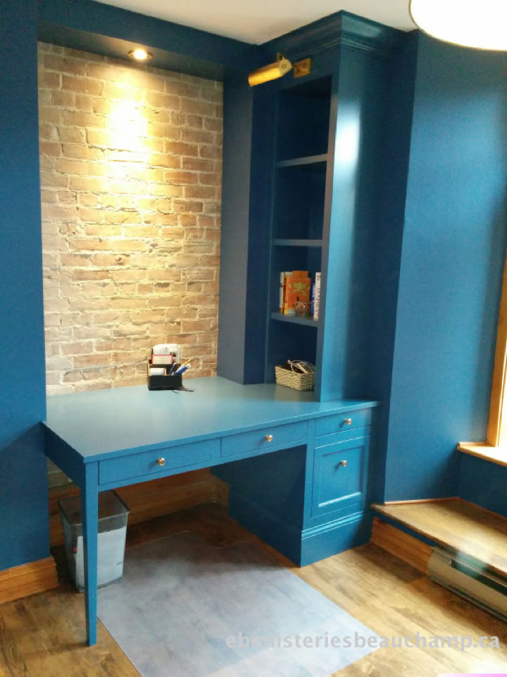 Bureau bleu intégré avec étagères, mur en briques apparentes, et lampe au-dessus.