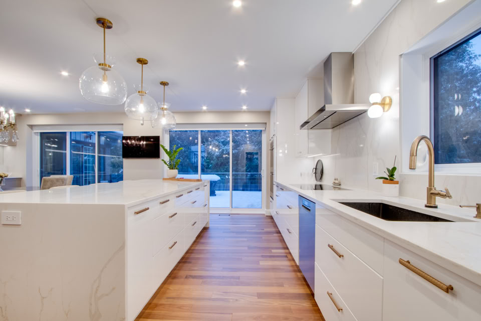 Modern kitchen with white cabinets, wooden floor, stainless steel appliances, and large windows.