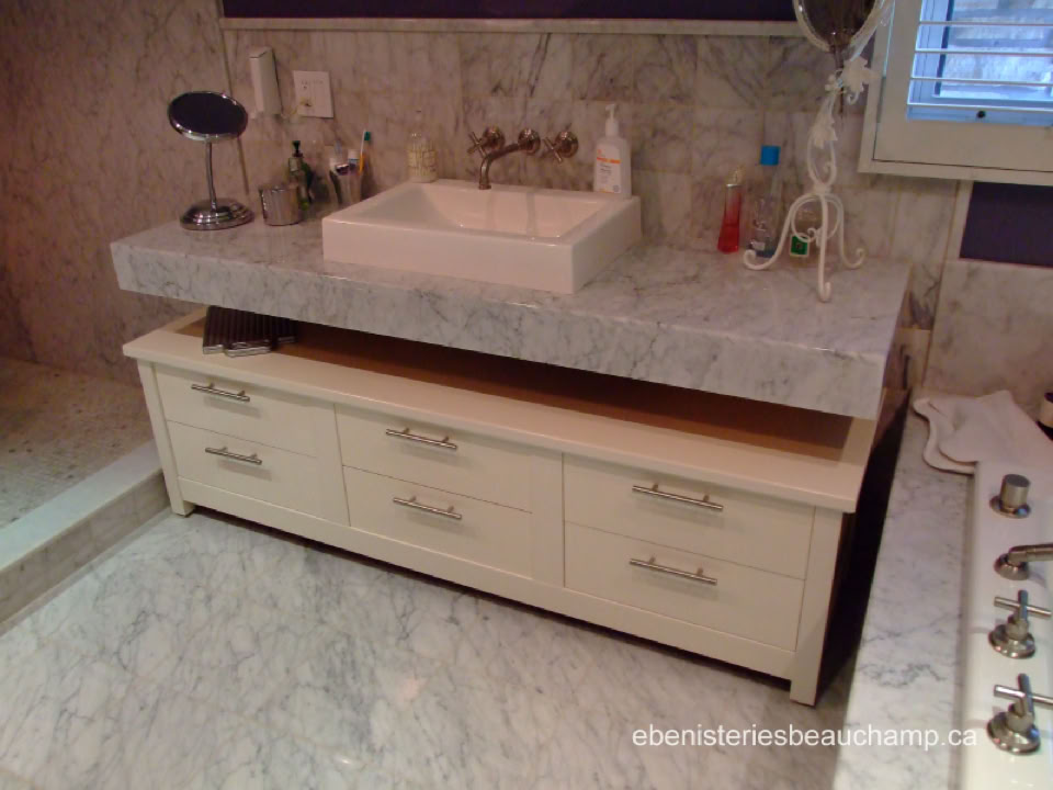 Salle de bain avec un lavabo rectangulaire sur un comptoir en marbre, des tiroirs en dessous, et divers articles de toilette autour.