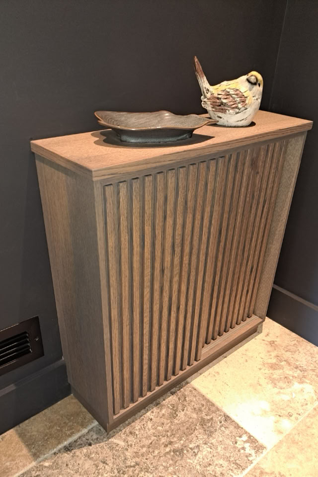 Un meuble en bois avec des rainures verticales, surmonté d'une assiette et d'une sculpture d'oiseau, posé sur un sol en carreaux.