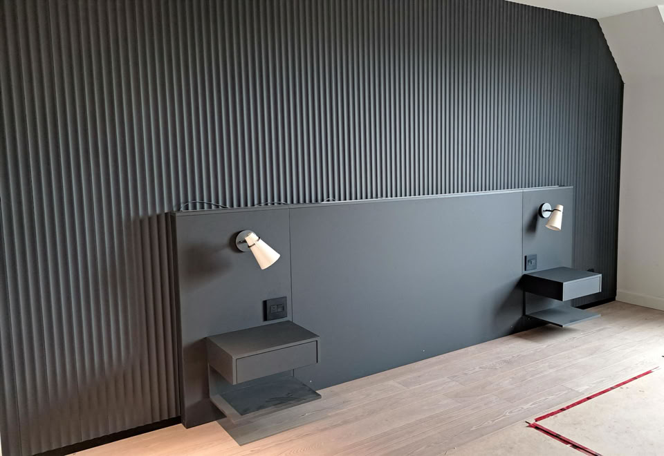 A modern bedroom with a dark textured accent wall, two mounted reading lights, and two floating bedside tables.