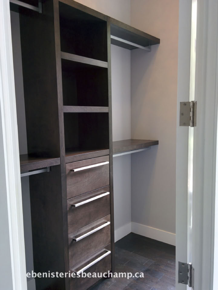 A small walk-in closet with dark wood shelving and drawers, featuring multiple shelves and a hanging rod.