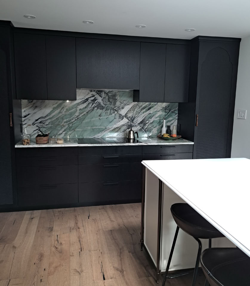 Modern kitchen with dark cabinets, a marble backsplash, and a white island with black stools.